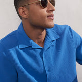 Man wearing a blue textured shirt and sunglasses against a plain background